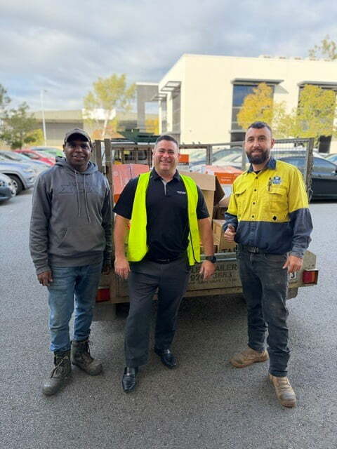 Three men are pictured standing in front of a trailer loaded with donations to Shalom House, including boxes of PPE and workshop supplies