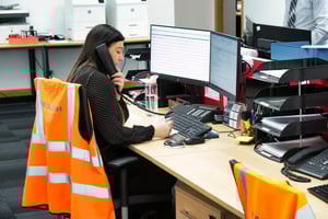 MacLean Internal Sales Representative Holly Stewart on the phone at her desk in Aberdeen office, wearing a high-visibility vest. Recognized for her life-saving actions on World Stroke Day.