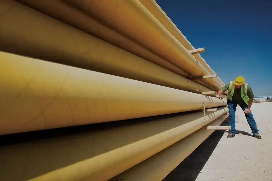 Image of a stack of yellow polyethylene pipe used in the gas utility sector. A worker to the right of the stack is inspecting the pipe.