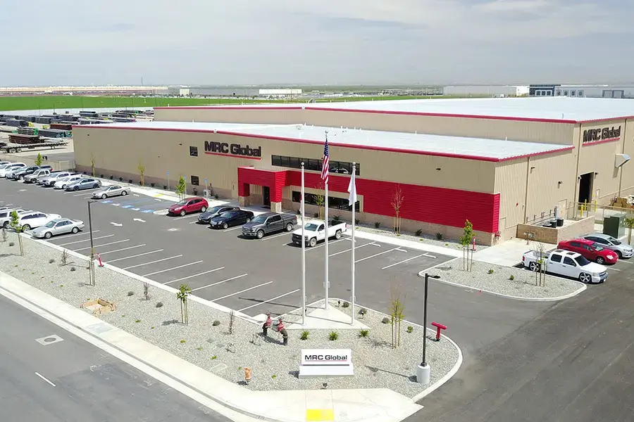 Image of an MRC Global branch location, showing the MRC Global logo on signs and the building, which has an attached warehouse and pipe yard.